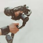 Close-up of a videographer holding a modern camera with stabilizer outdoors. Capturing high-quality footage.